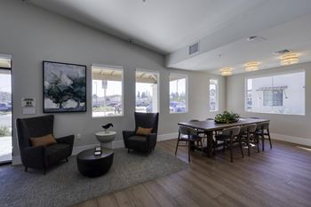 A living room with a grey sofa, a black coffee table, a dining table with chairs and a painting on the wall.